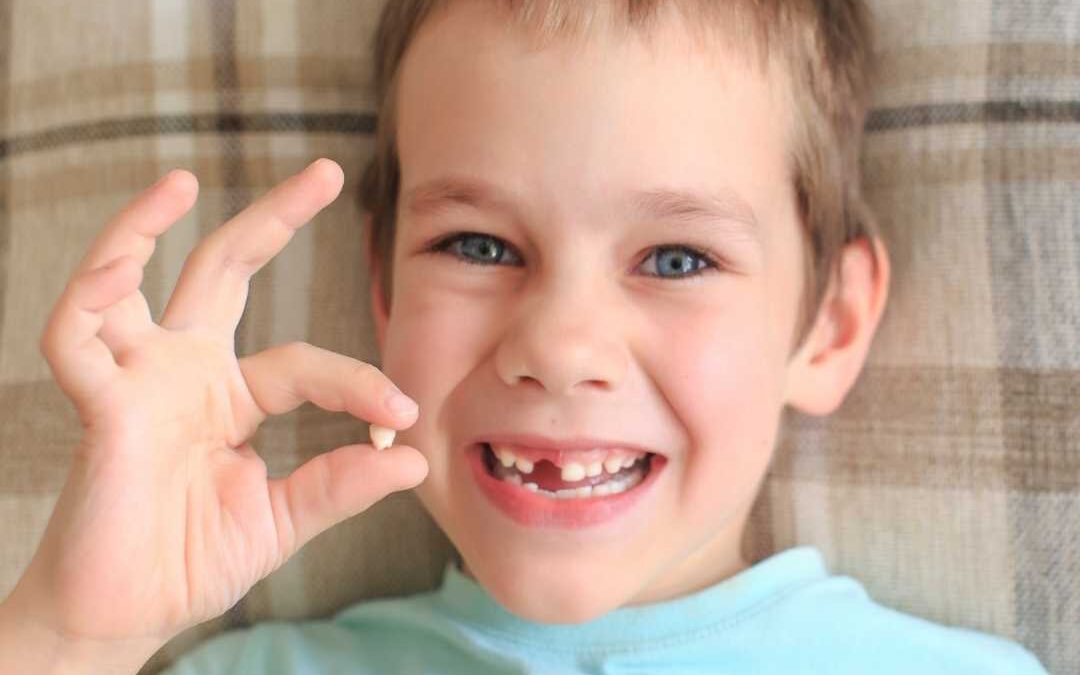 bambino di sei anni mostra il dentino da latte che gli è caduto